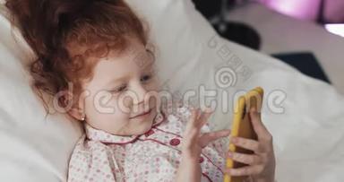有趣的红头发小女孩与黄色智能<strong>手机</strong>躺在床上和使用智能<strong>手机</strong>。 沟通，播放，<strong>APP</strong>..